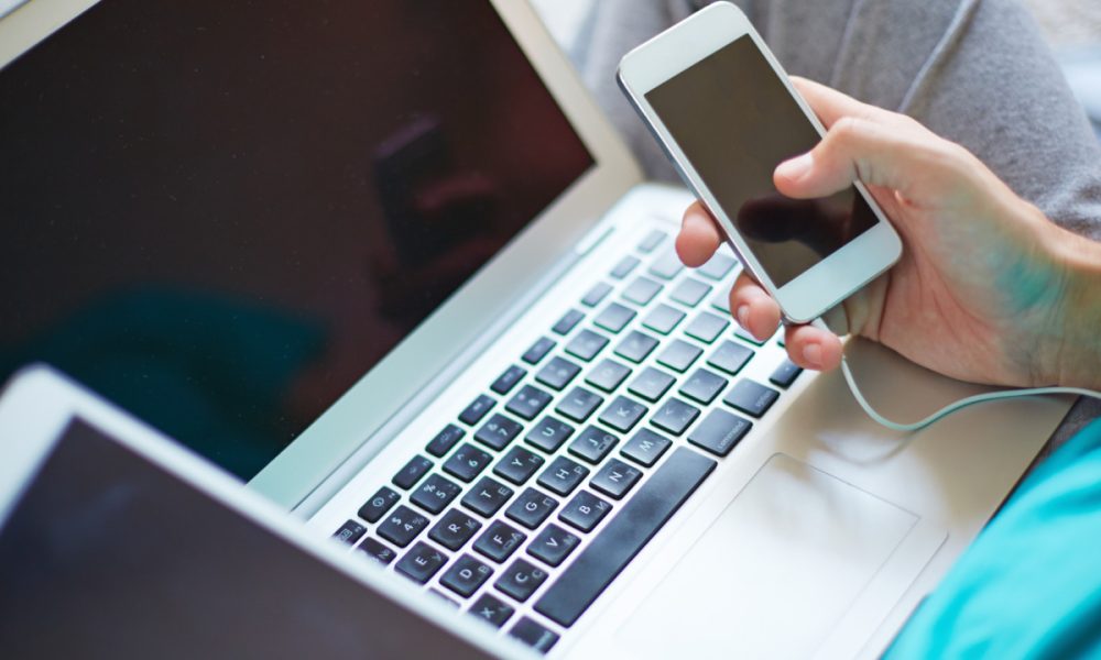 Hand of man with cellphone over open laptop