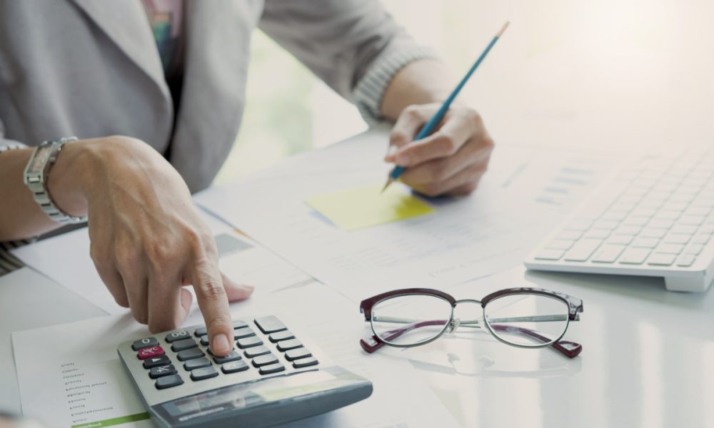 Close up Business woman using calculator and laptop for do math finance on wooden desk in office and business working background, tax, accounting, statistics and analytic research concept